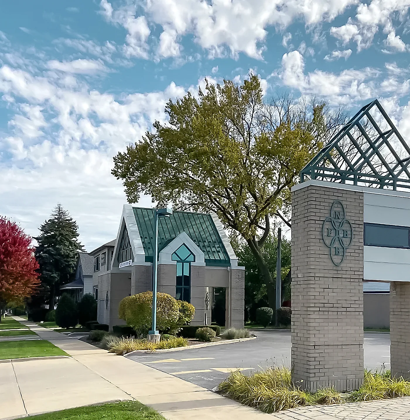 Most recement image of the First National Bank of Brookfield, with their green stained glass roof on top of their building and greenery around the building.