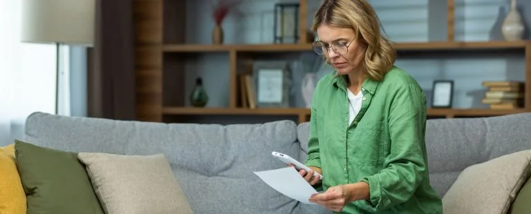 A person is looking worriedly at a suspicious paper, ready to call someone about it.