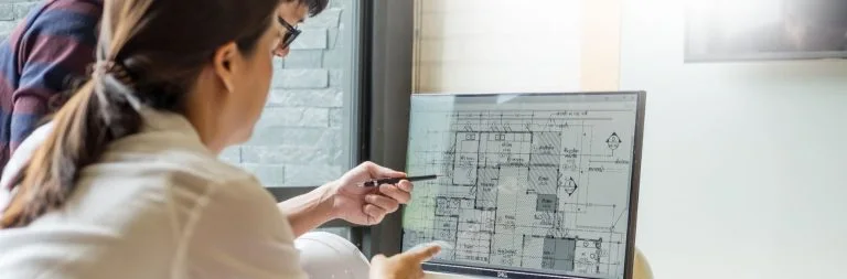 Construction contractor explains project plans on laptop screen to loan broker.